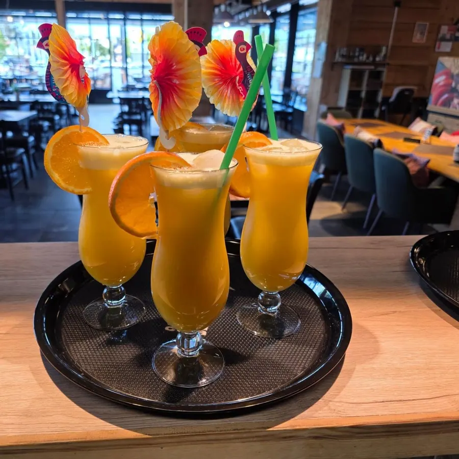 Drei Cocktails auf dem Tablett, dahinter der Gastraum
