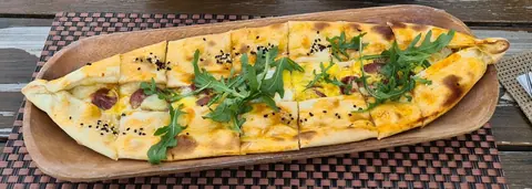 Pide mit Sucuk, Ei, Käse und Rucola auf einem Holzbrett