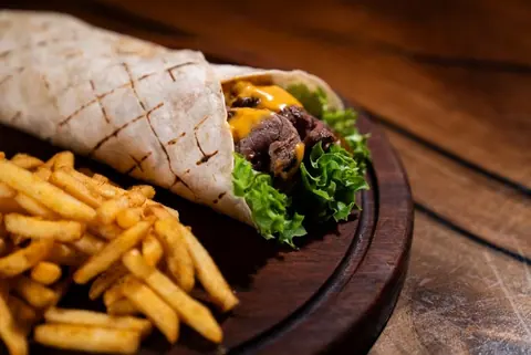 Fleisch-Wrap mit Pommes auf dunklem Holzbrett