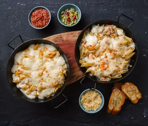 Zwei Pfannen mit überbackenen Nudeln und Käse