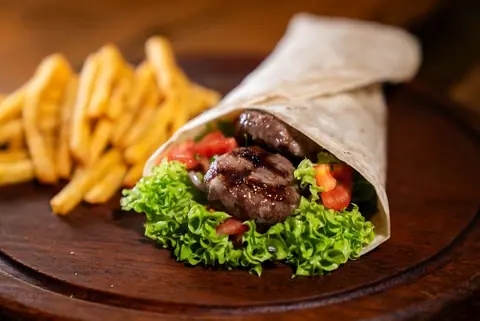 Gegrillter Wrap mit Fleisch und Salat, dazu Pommes