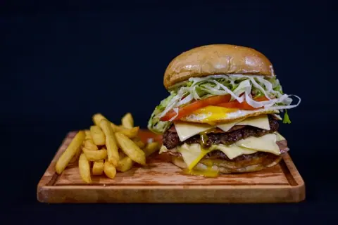 Doppelter Cheeseburger mit Pommes auf einem Holzbrett
