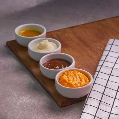 Kleine Schälchen mit Mayo, Ketchup und weiteren Soßen auf dem Holzbrett